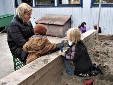 Børn og voksen i sandkasse